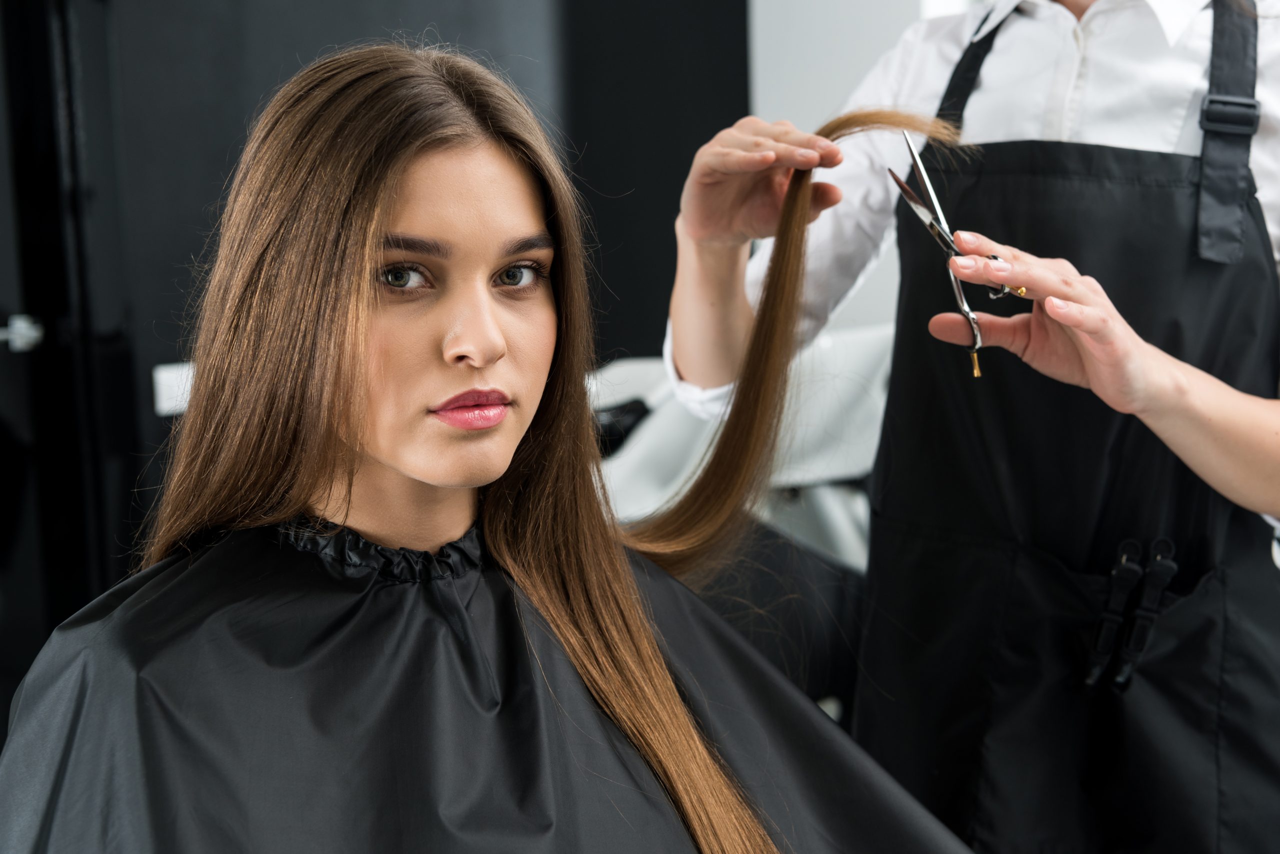 stylist cutting hair of beautiful young woman